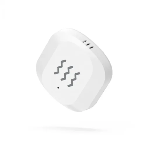 WOOX vibrationssensor i hvid, afrundet firkant med bølgeikon og lille LED på forsiden og tre ventilationsåbninger på siden.